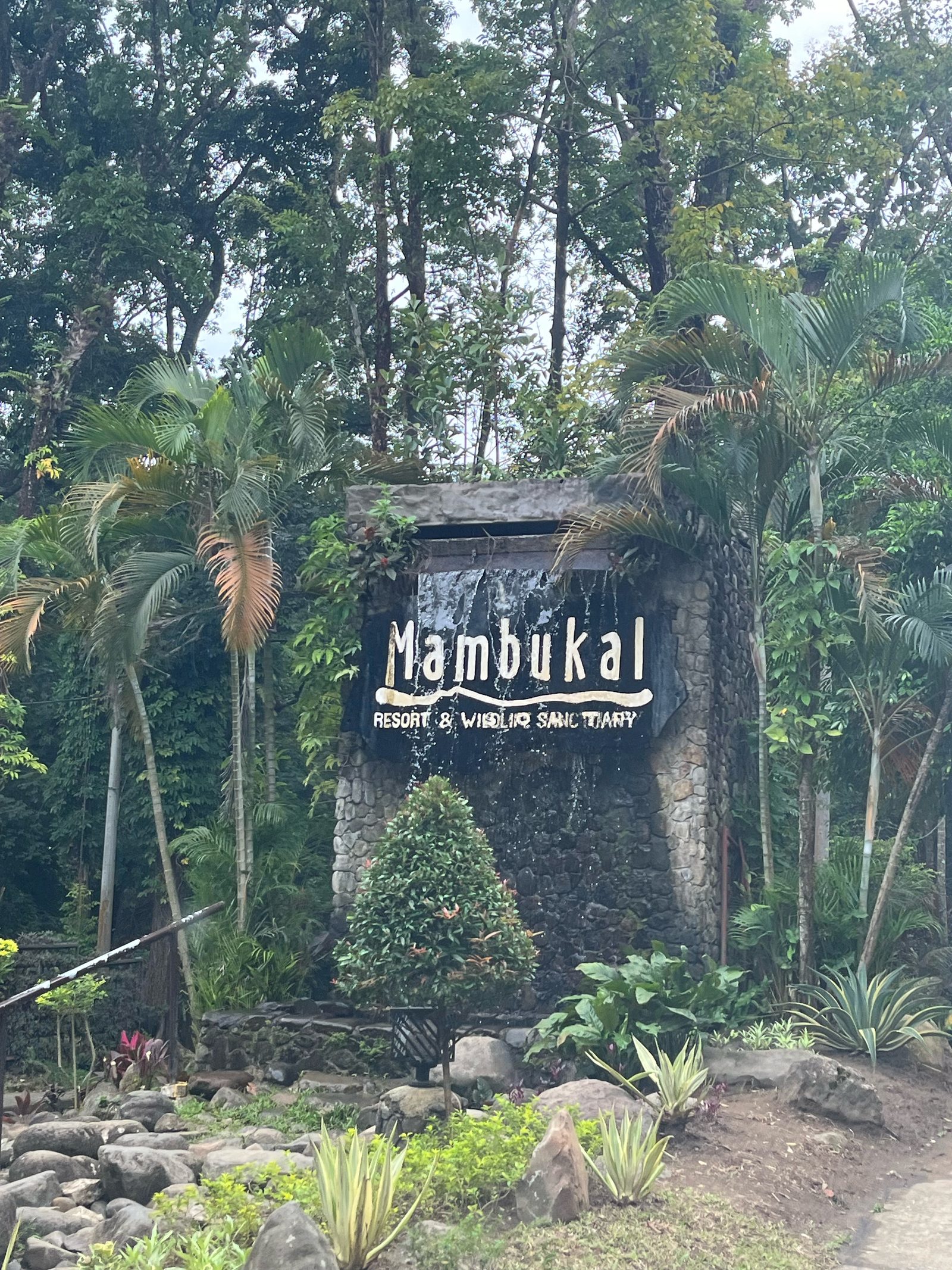 Stone entrance sign at Mambukal Resort and Wildlife Sanctuary, with water running down the rock face.