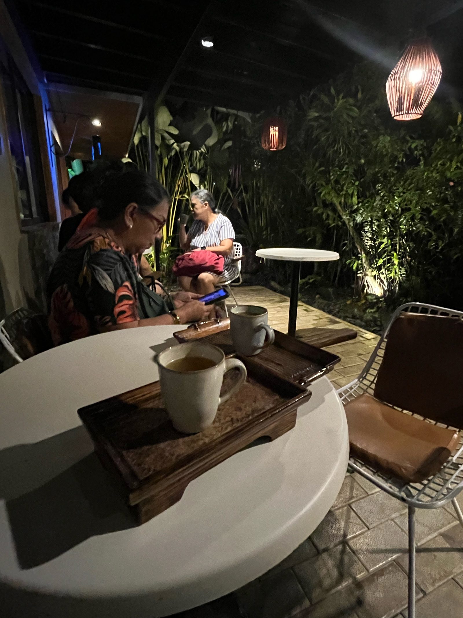 Two guests at Spa Natura's Tea Garden, holding glasses of ginger tea under a woven lantern.