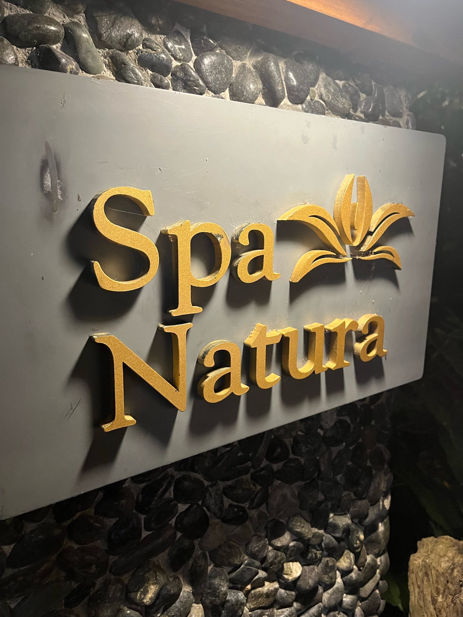 Gold Spa Natura sign on a stone wall, with a small tree in front of it.